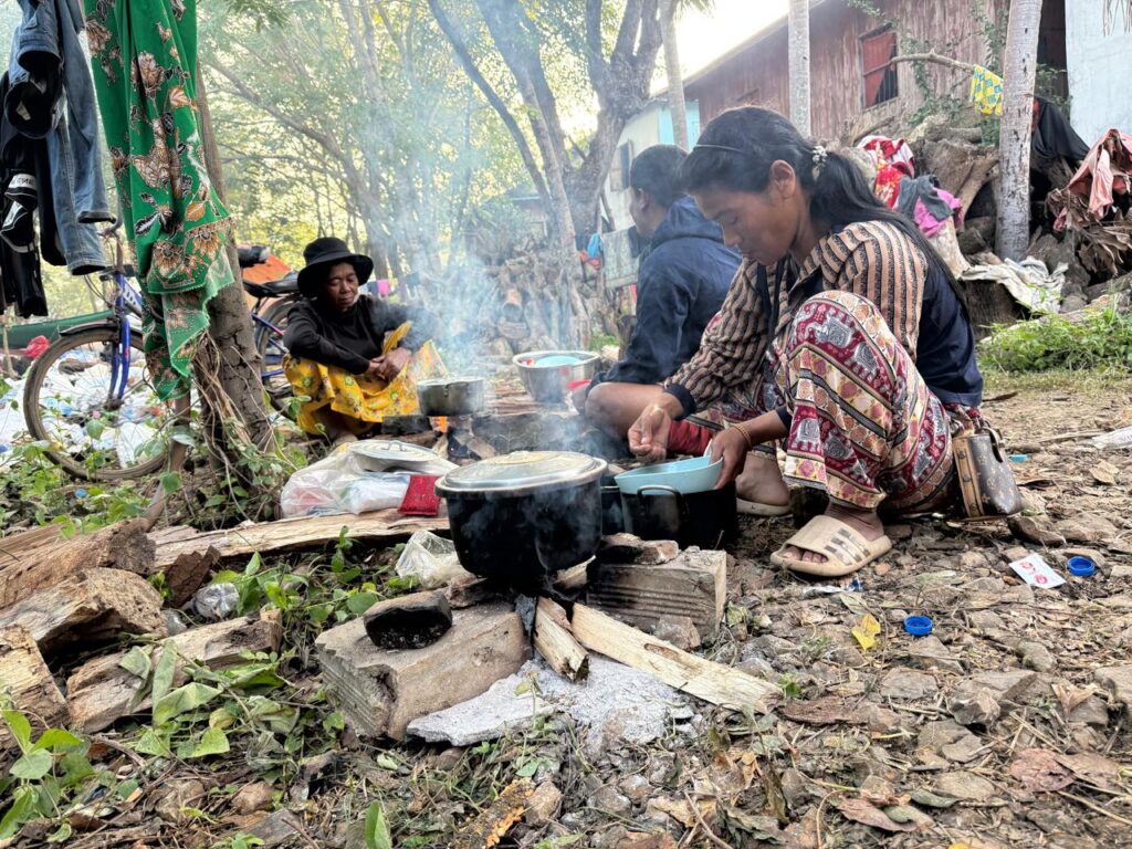A woman crouches to cook her lunch over a campfire inside a resettlement camp at Khnah Romea pagoda in XXX province on December 16, 2025. (Mech Dara/Mekong Independent)