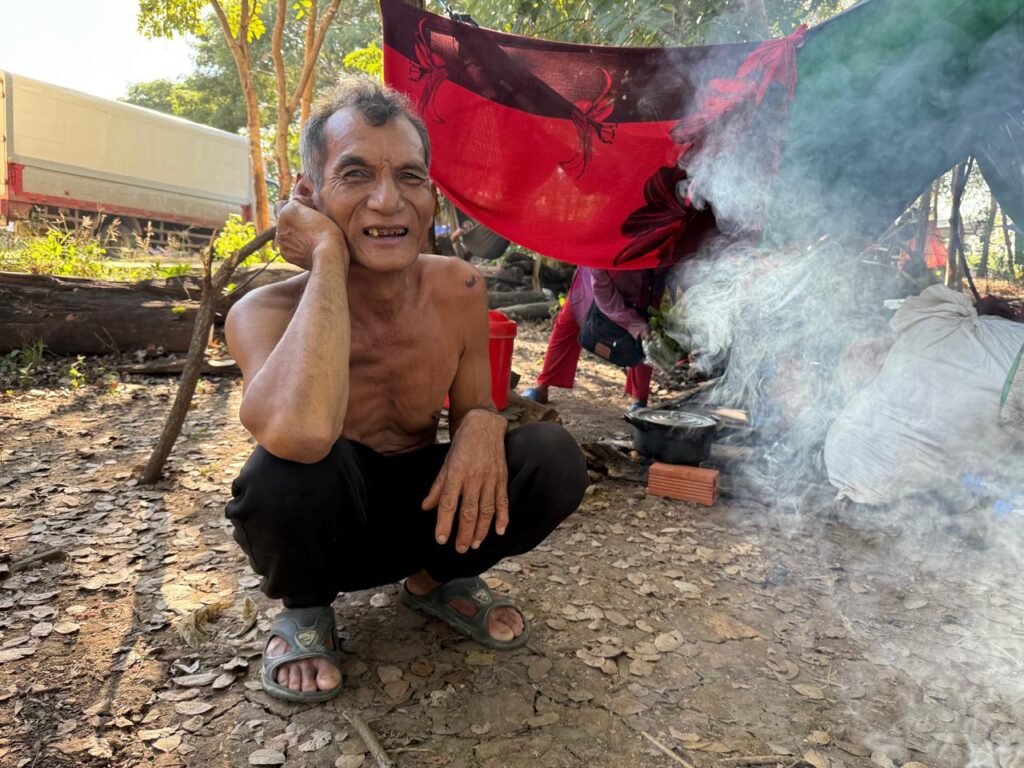 Rath, a 58-year-old construction worker who worked at a development in Banteay Meanchey's O'Bei Choan district, sits beside a fire at a temporary resettlement camp in Banteay Meanchey's Ou Chrouv commune. (Mech Dara/Mekong Independent)