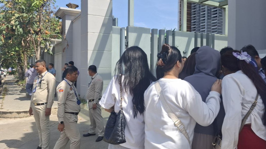 Civilians crowd around a man who met with the National Bank of Cambodia to discuss funds locked into a Huione Pay account, outside the entrance to the central bank's Phnom Penh headquarters on Dec. 8, 2025. (Danielle Keeton-Olsen/Mekong Independent/Creative Commons)