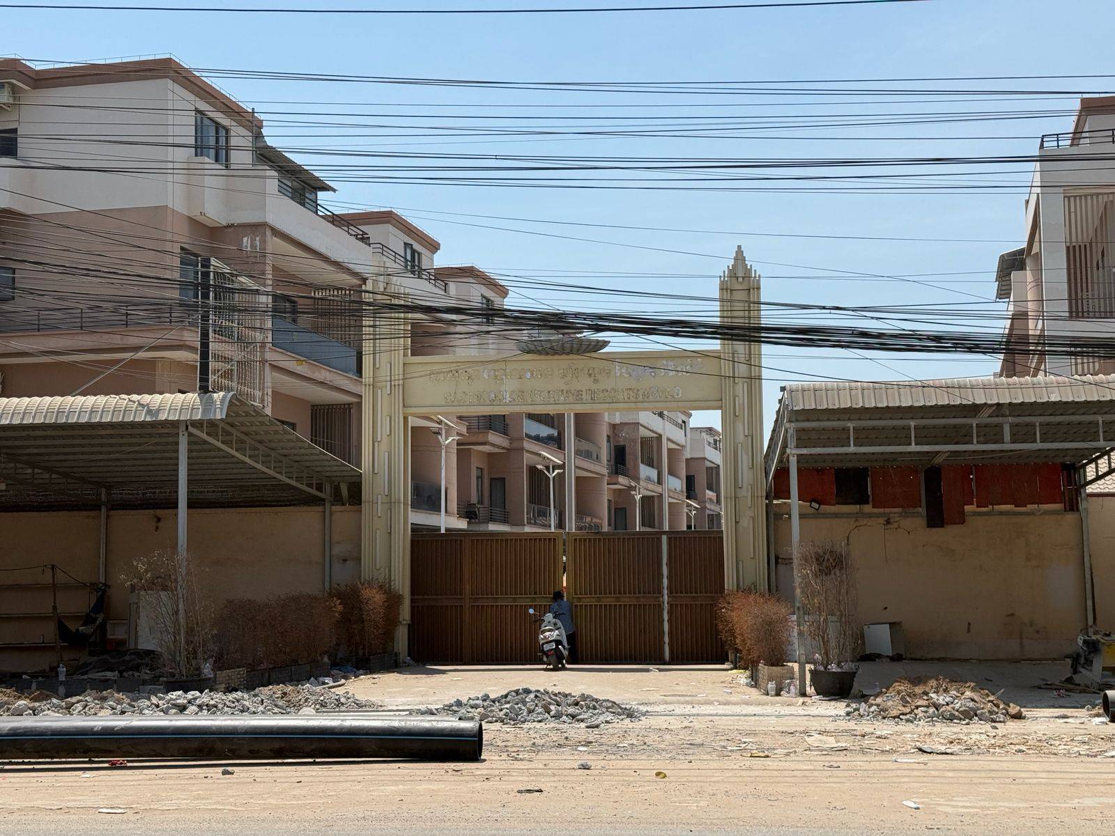 A man tries to get through the gate of the Golden Fortune World Resort Casino, which removed its sign and appeared abandoned, in Cambodia's Sampov Poun city on Feb. 20, 2026. (Mech Dara/Mekong Independent/Creative Commons)